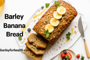 A freshly baked healthy banana bread with barley loaf topped with banana slices, oats, and honey, surrounded by yogurt, berries, and a knife on a bright kitchen table with the text Barley Banana Bread and barleyforhealth.com.